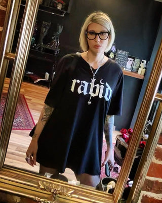 A person taking a mirror selfie wearing an oversized black t-shirt with the word 'rabid' printed in white gothic lettering across the chest, paired with black glasses and a silver necklace.